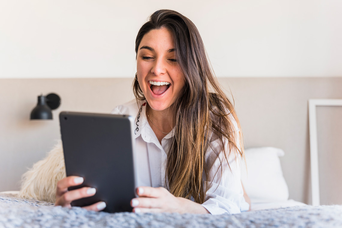 Mujer sonriendo con tablet en la cama de un GF: Corporativa.