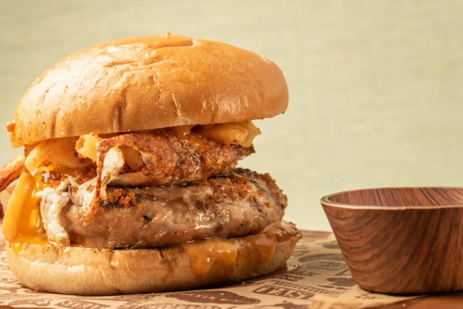 a hamburger sits on a table next to a bowl that says tasty