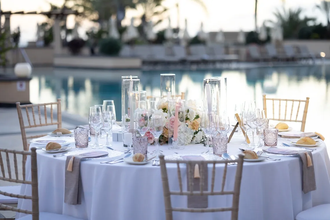 Mesa decorada para evento corporativo con flores y copas junto a piscina.