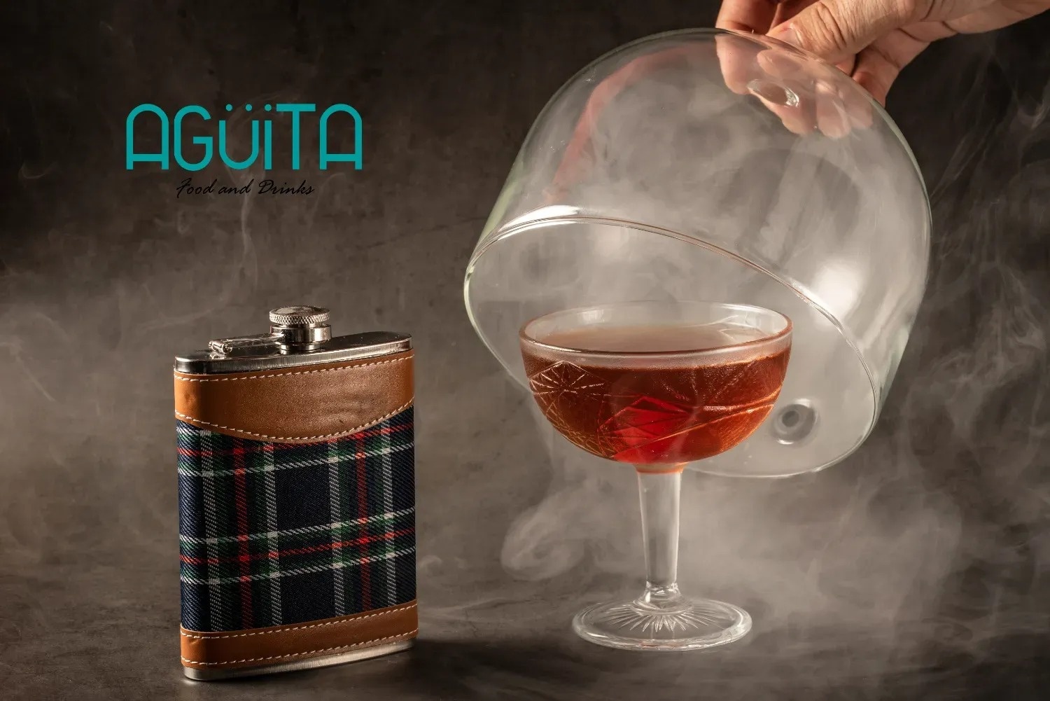 a glass with smoke coming out of it next to a flask that says aguila