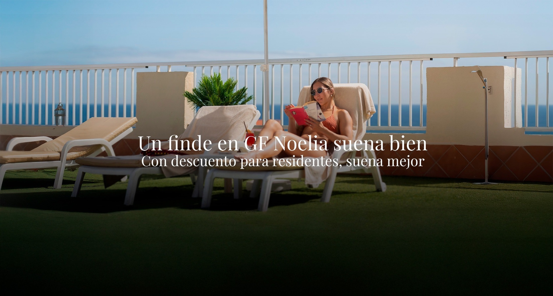 una mujer con un vestido blanco y gafas de sol está sentada en la playa