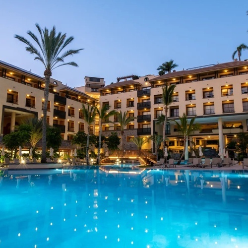 una gran piscina está rodeada de palmeras frente a un gran hotel