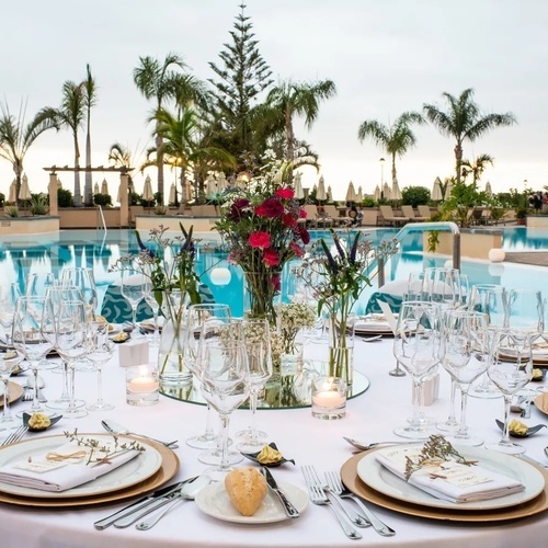 una mesa con platos , copas de vino y velas frente a una piscina