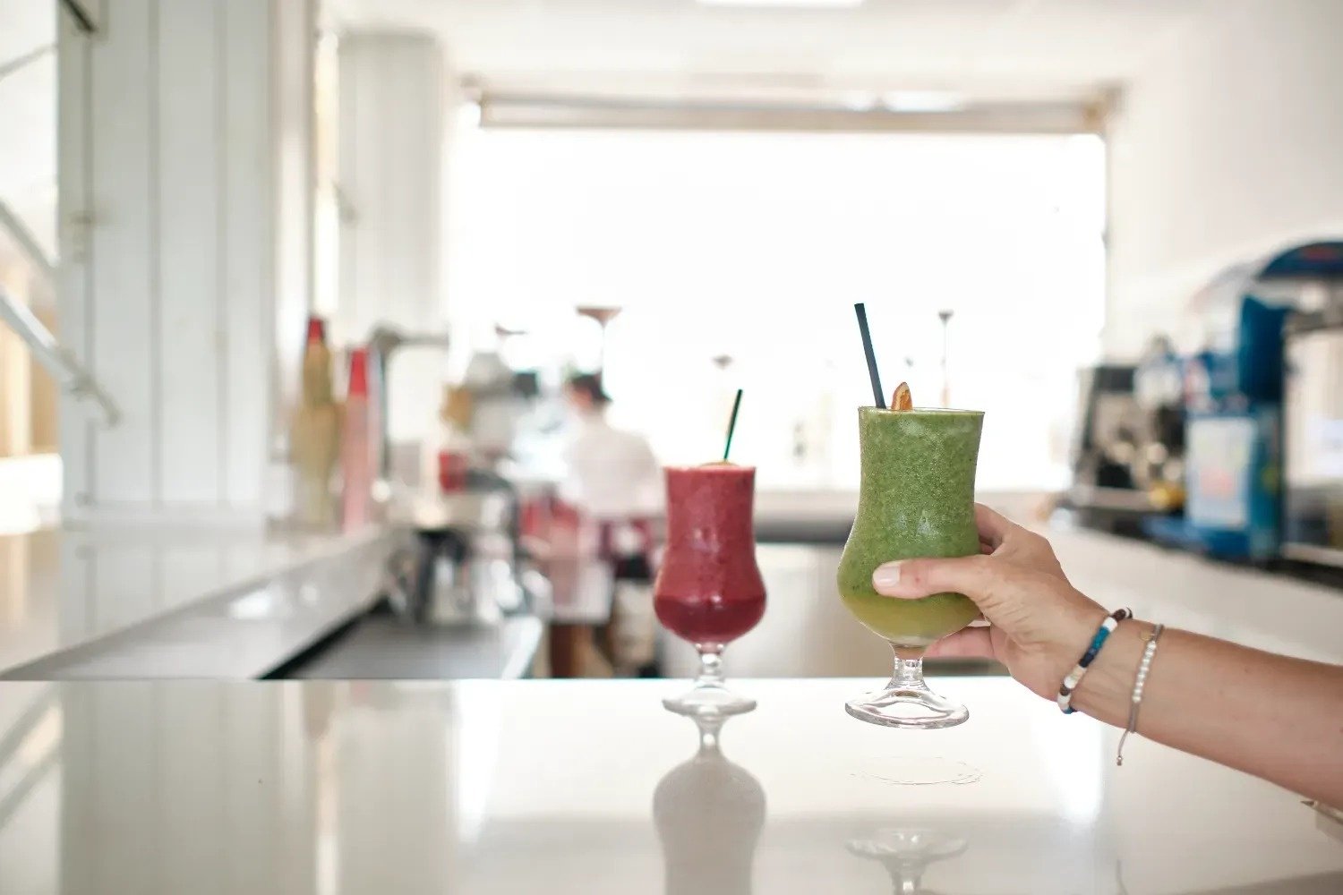 una persona sostiene un batido verde junto a un batido rojo