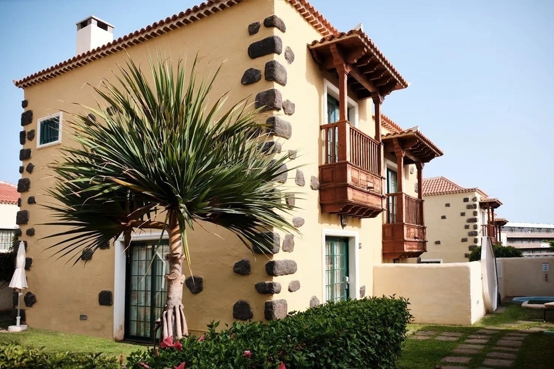 una casa amarilla con balcones de madera y palmeras