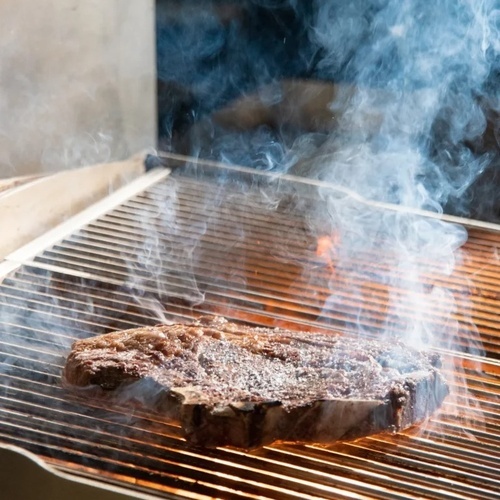un bistec se está cocinando en una parrilla con humo saliendo de ella