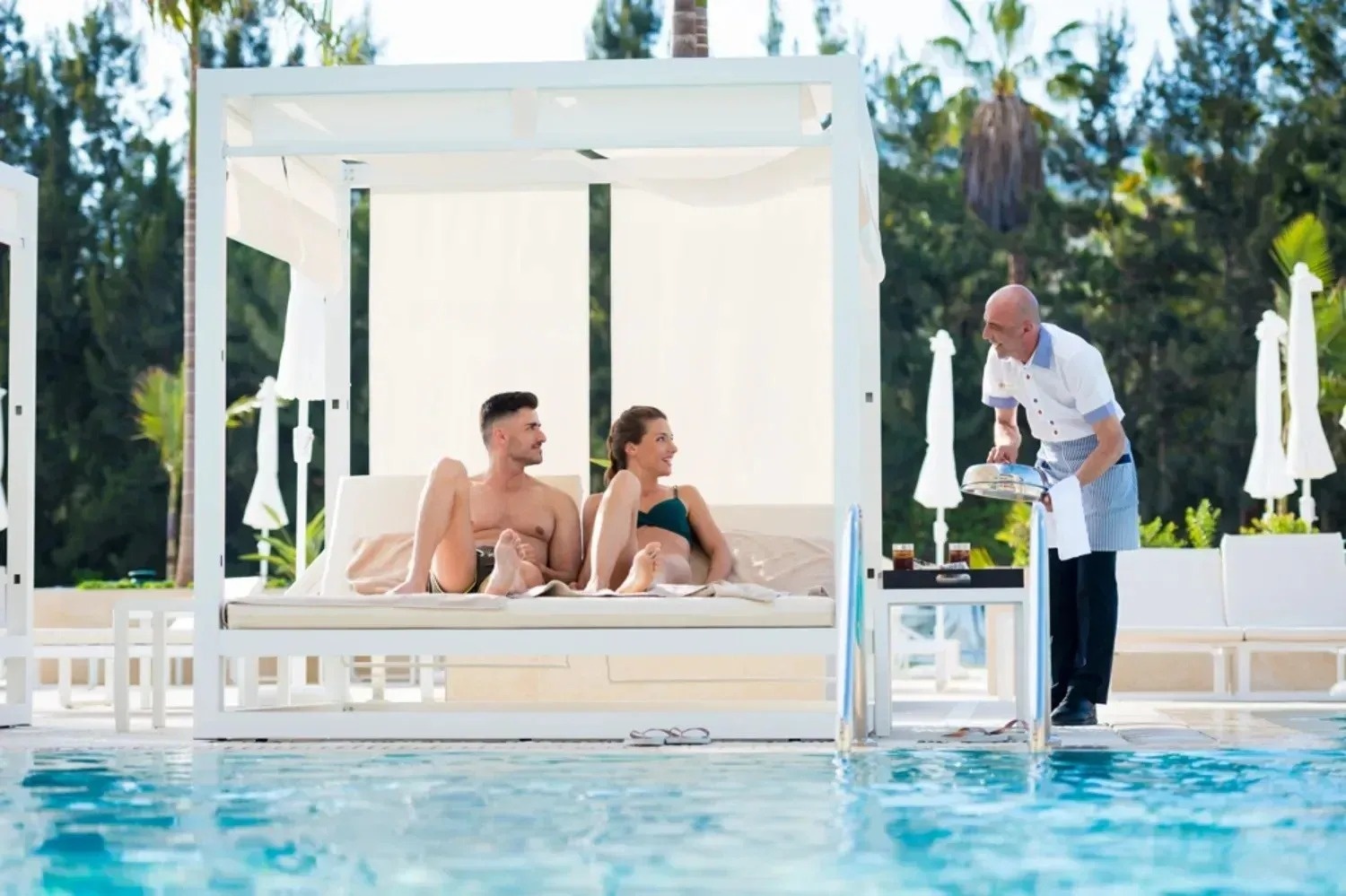 un hombre y una mujer están sentados en una cama junto a una piscina