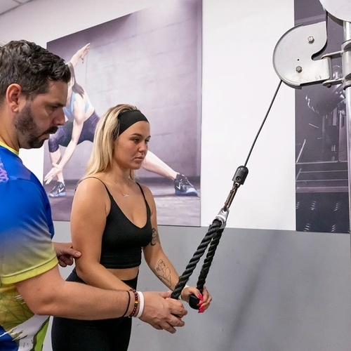 a man in a blue and yellow shirt is teaching a woman how to use a machine
