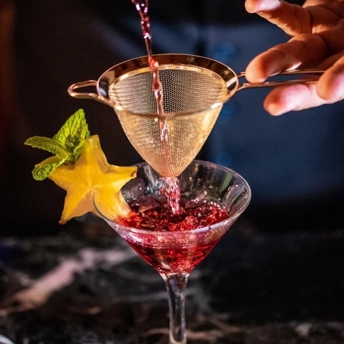 un barman está vertiendo un cóctel rojo a través de un colador