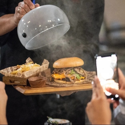 un hombre sostiene una bandeja de madera con una hamburguesa y papas fritas encima