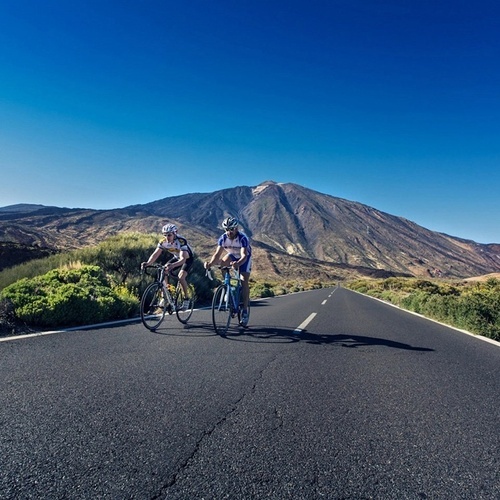 dos personas andan en bicicleta por una carretera con una montaña en el fondo