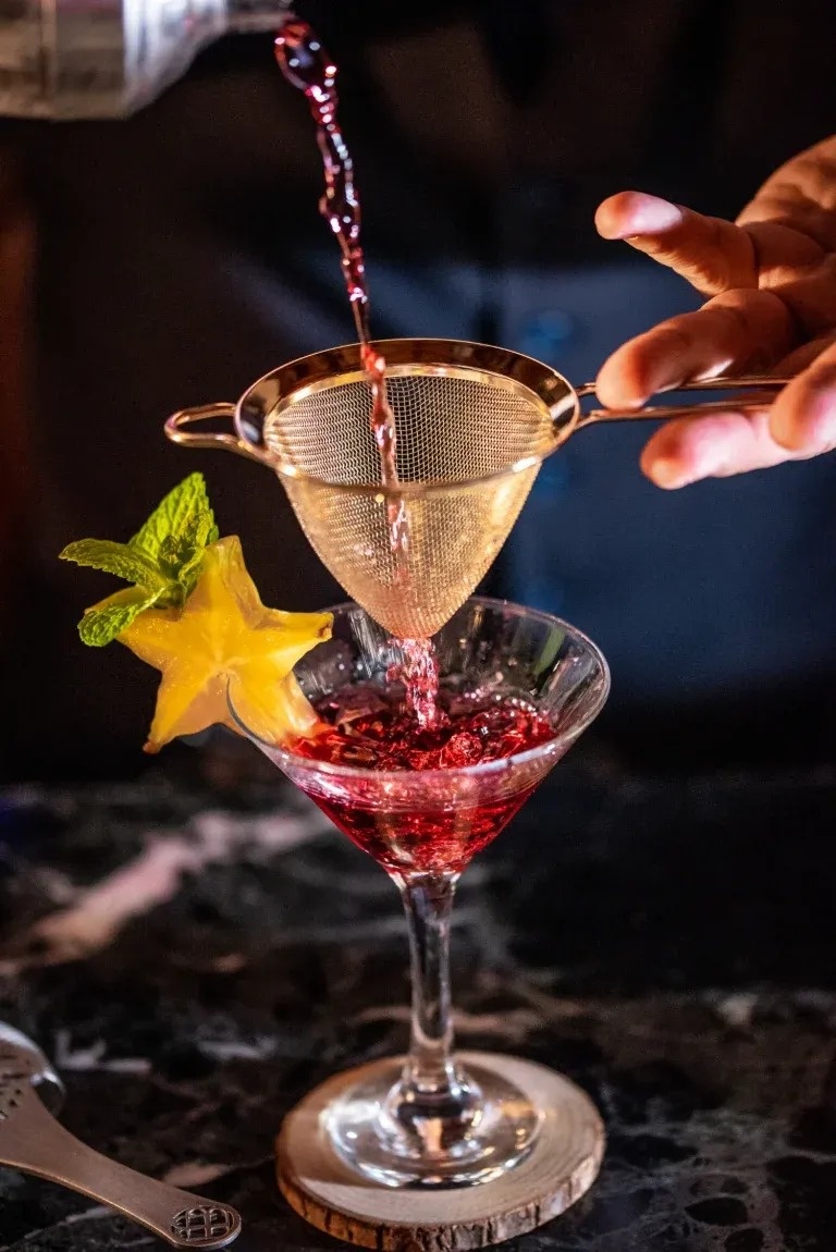 a person pouring a drink through a strainer into a martini glass