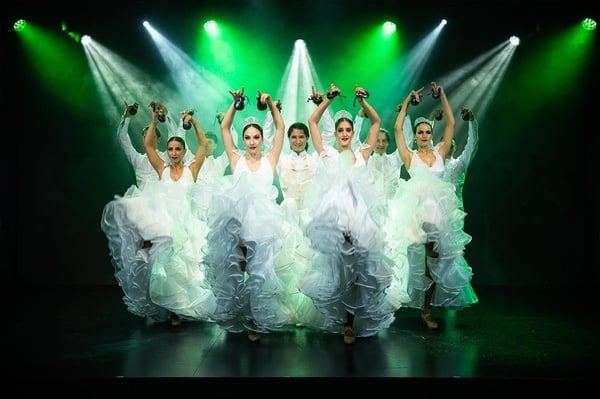 un grupo de mujeres en vestidos blancos bailan en un escenario con luces verdes