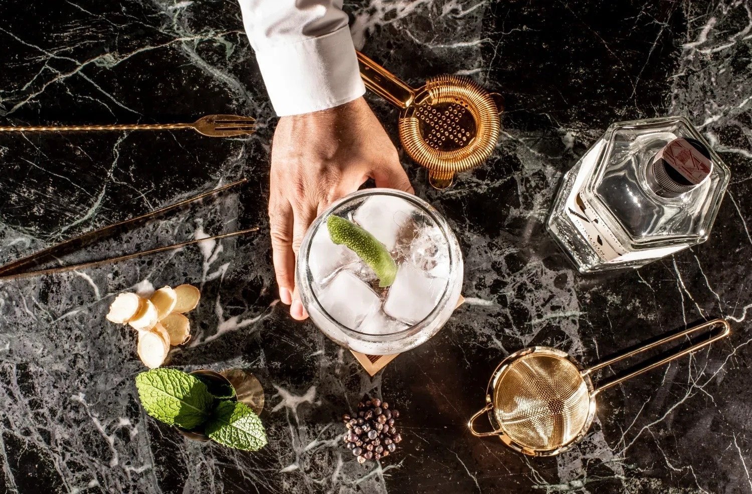 a bartender prepares a drink with a bottle of gin in the background