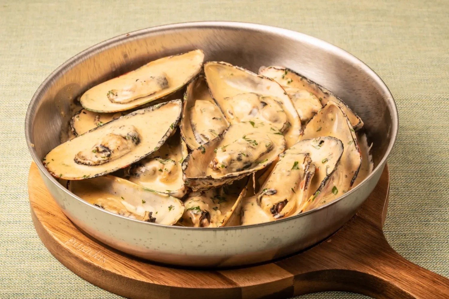 a pan of mussels is on a wooden cutting board