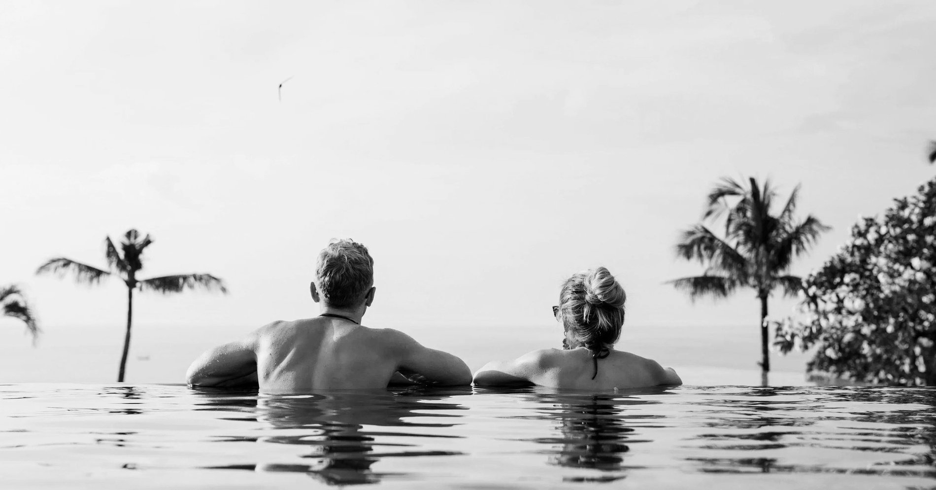 un hombre y una mujer están sentados en una piscina infinita mirando al océano=s1900