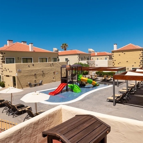 a swimming pool surrounded by chairs and umbrellas with a playground in the middle