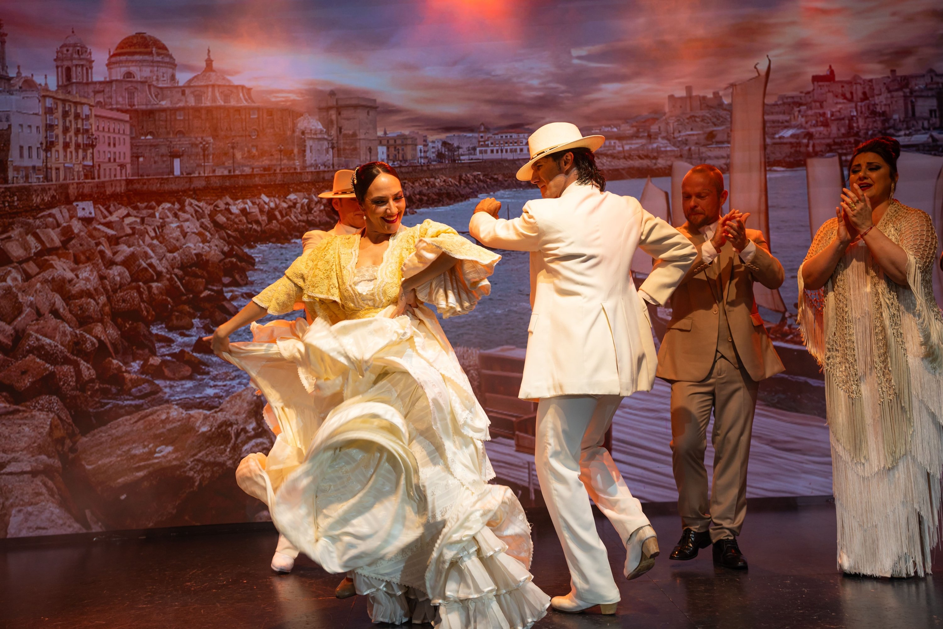 un grupo de hombres y mujeres en vestidos blancos con lunares rojos están actuando en un escenario