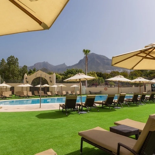 a swimming pool surrounded by chairs and umbrellas with mountains in the background