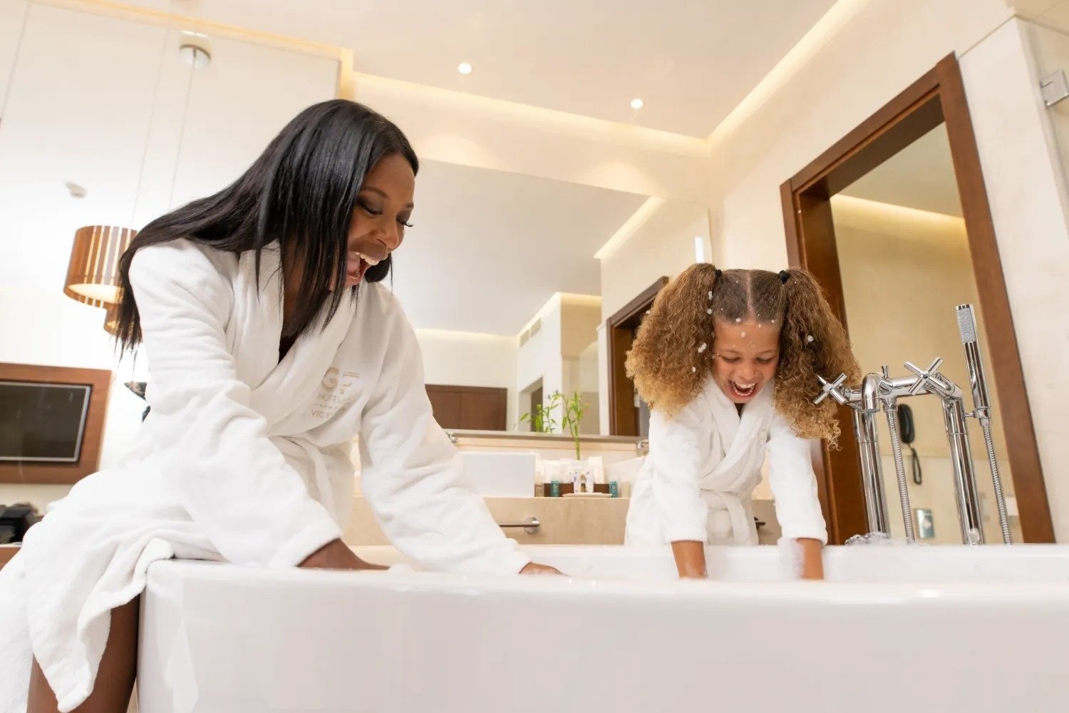 a woman and a little girl are playing in a bathtub and the woman is wearing a robe that says ' spa '