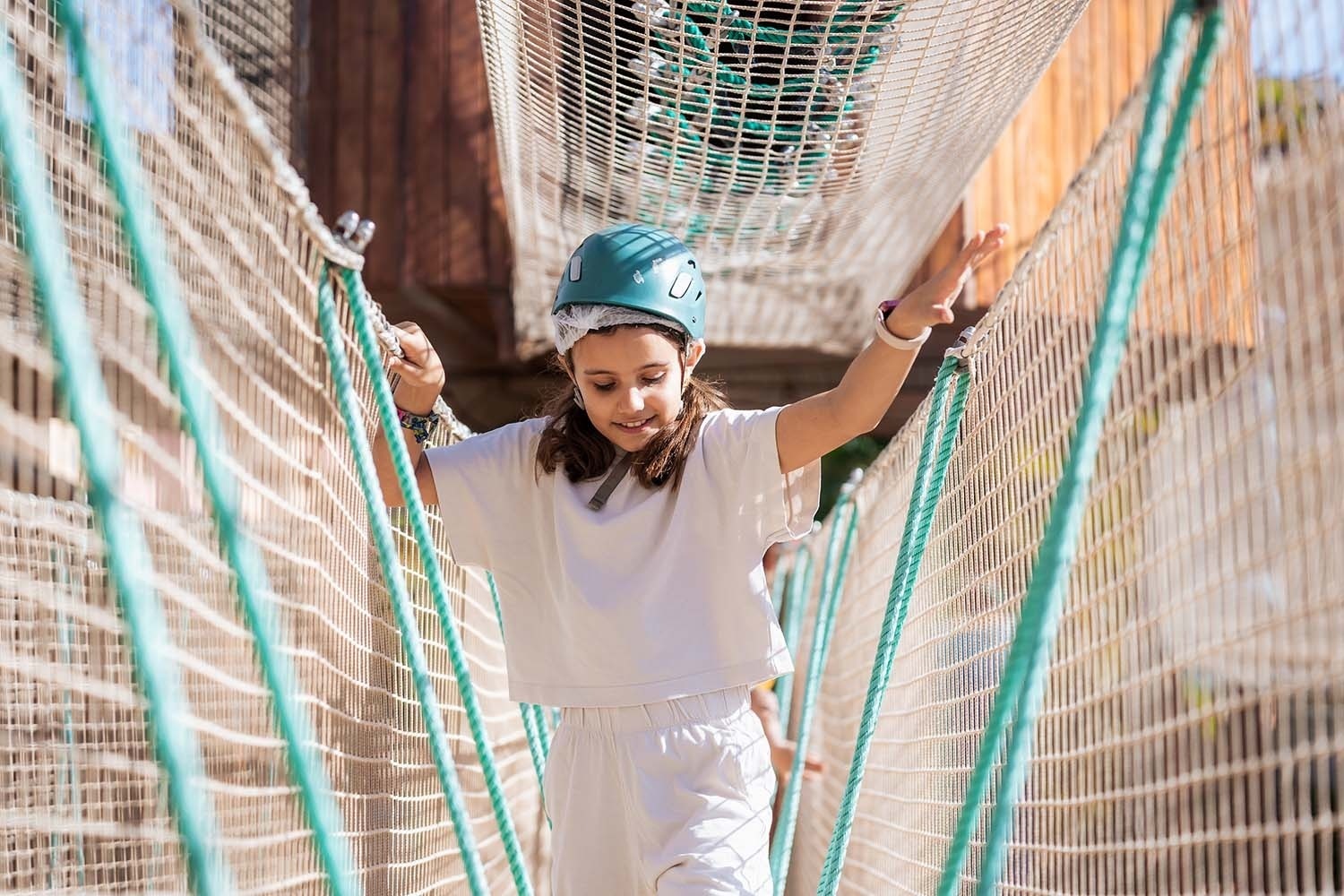 a girl wearing a blue helmet is walking across a rope bridge