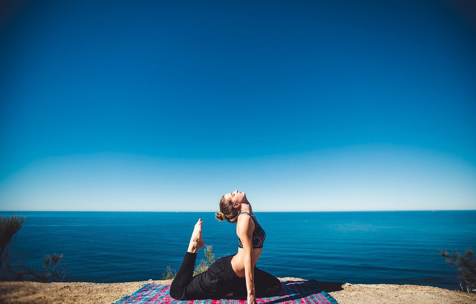 una mujer se sienta en una pose de yoga frente al océano