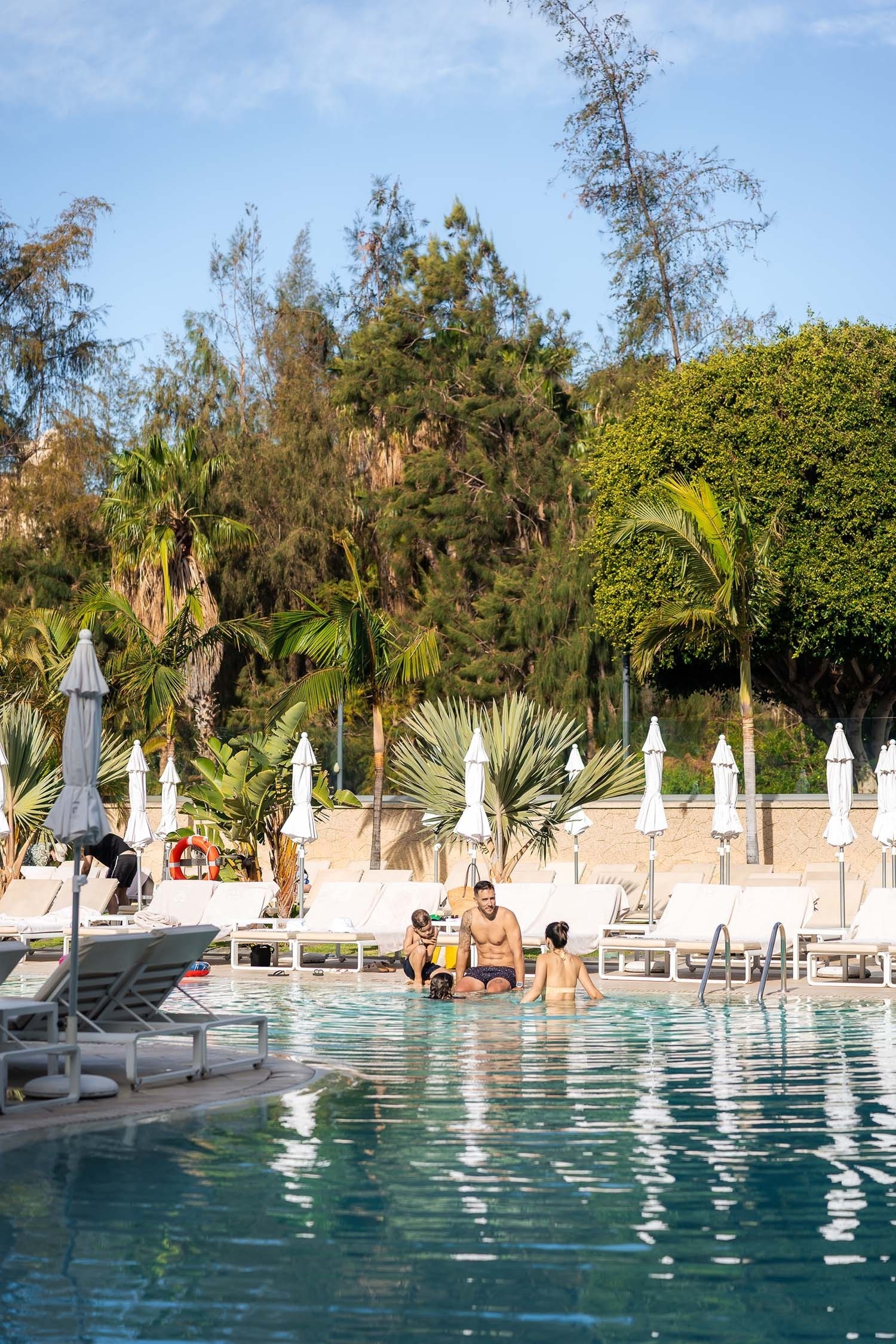 a man and woman sit in a swimming pool surrounded by chairs and umbrellas
