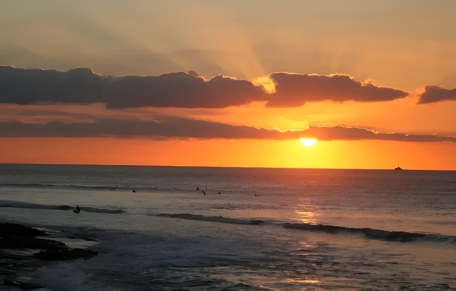 el sol se pone sobre el océano y los surfistas están en el agua