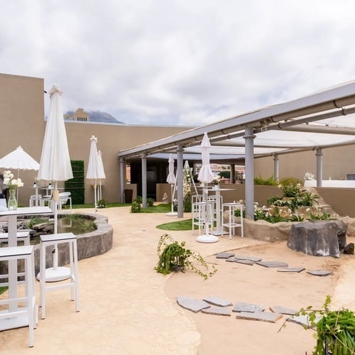 un patio con mesas y sillas y sombrillas blancas