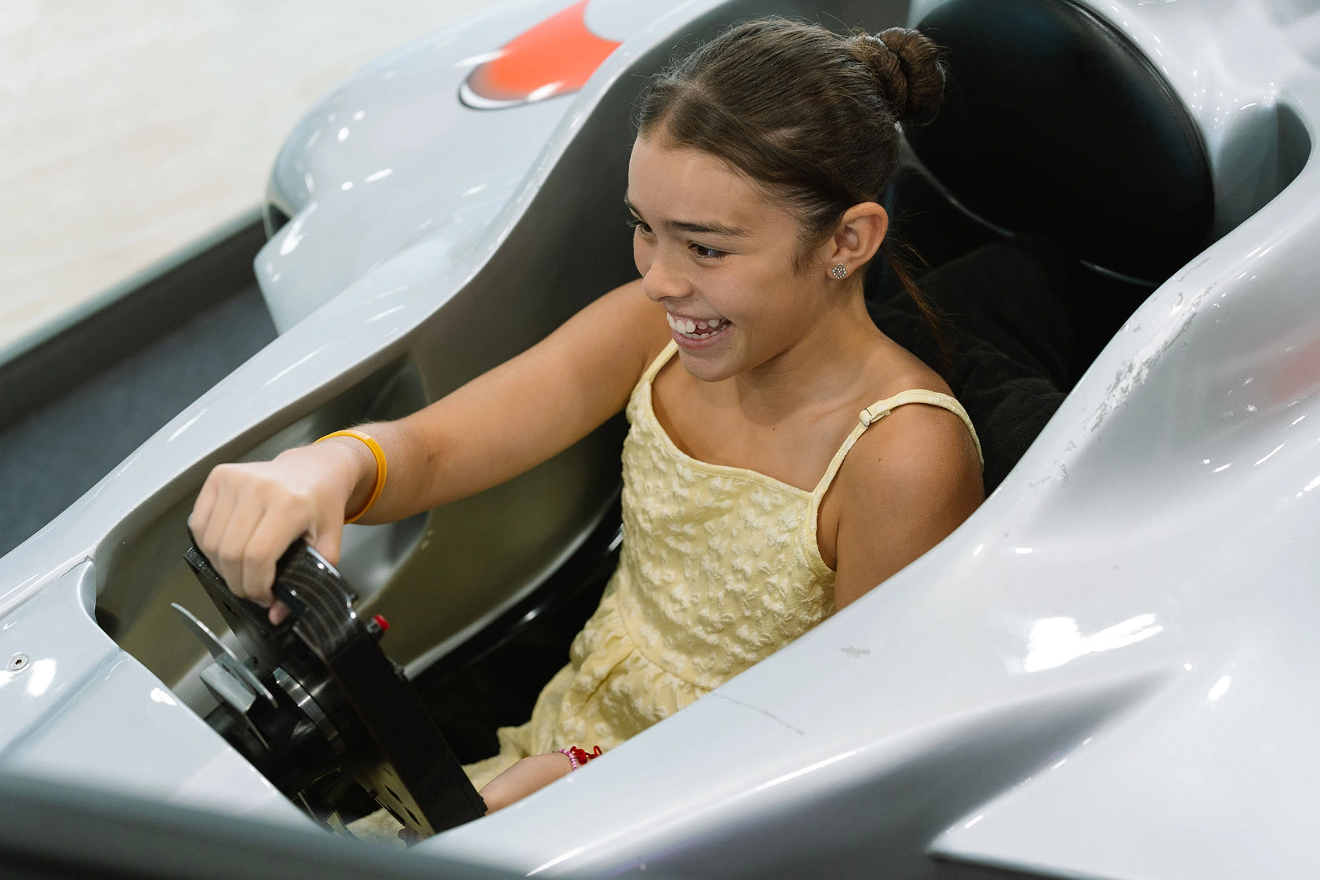 Niña sonriente en un auto de carreras de juguete, perfecta para la diversión familiar en nuestro hotel. GF: Victoria