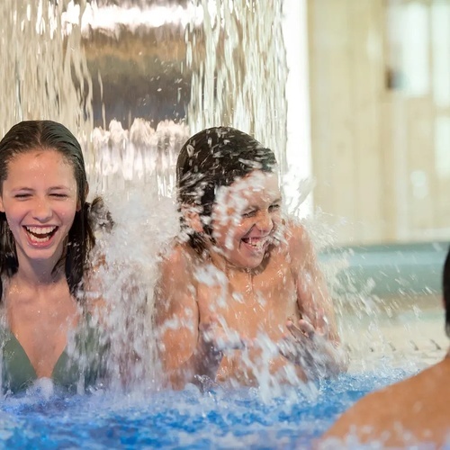 un hombre y dos niños se divierten bajo una cascada en una piscina