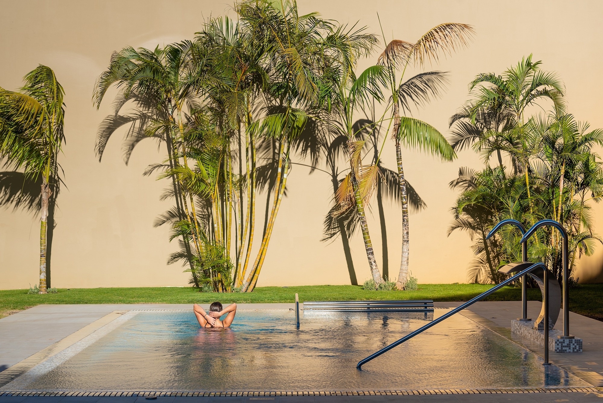 una mujer se sienta en una piscina rodeada de palmeras