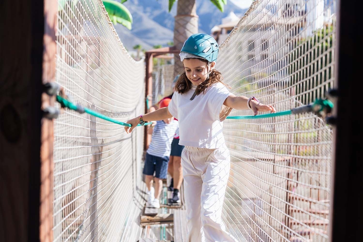 a girl wearing a blue helmet is walking across a rope bridge