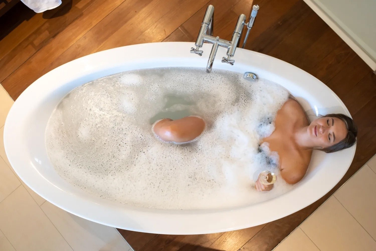 a woman is laying in a bathtub with foam and holding a glass of wine