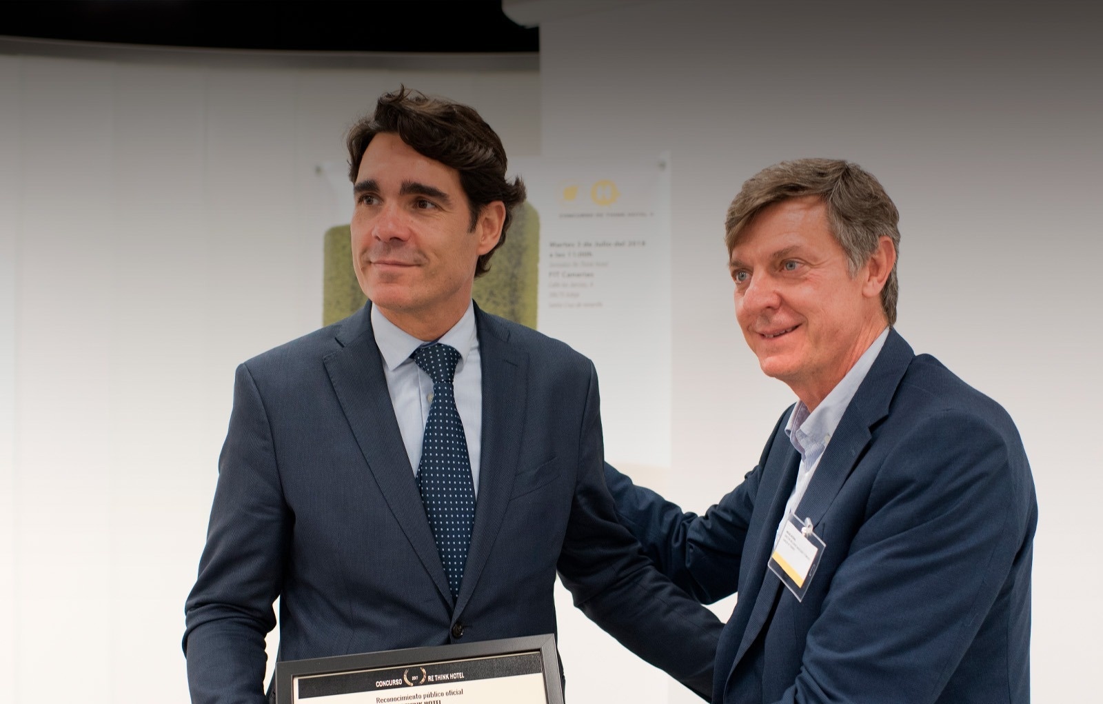 dos hombres se dan la mano y uno de ellos sostiene un trofeo que dice premio