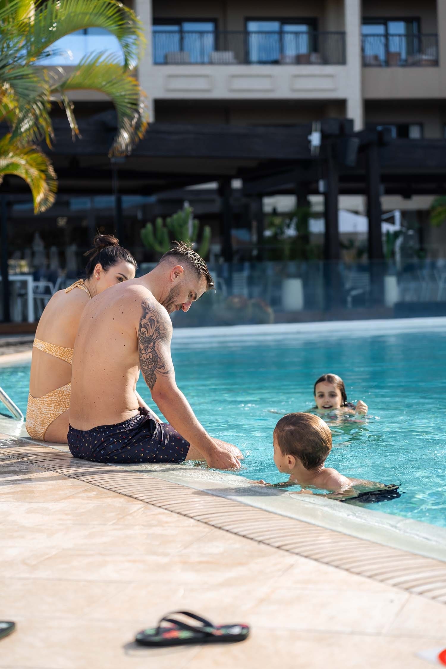 a family sits on the edge of a swimming pool
