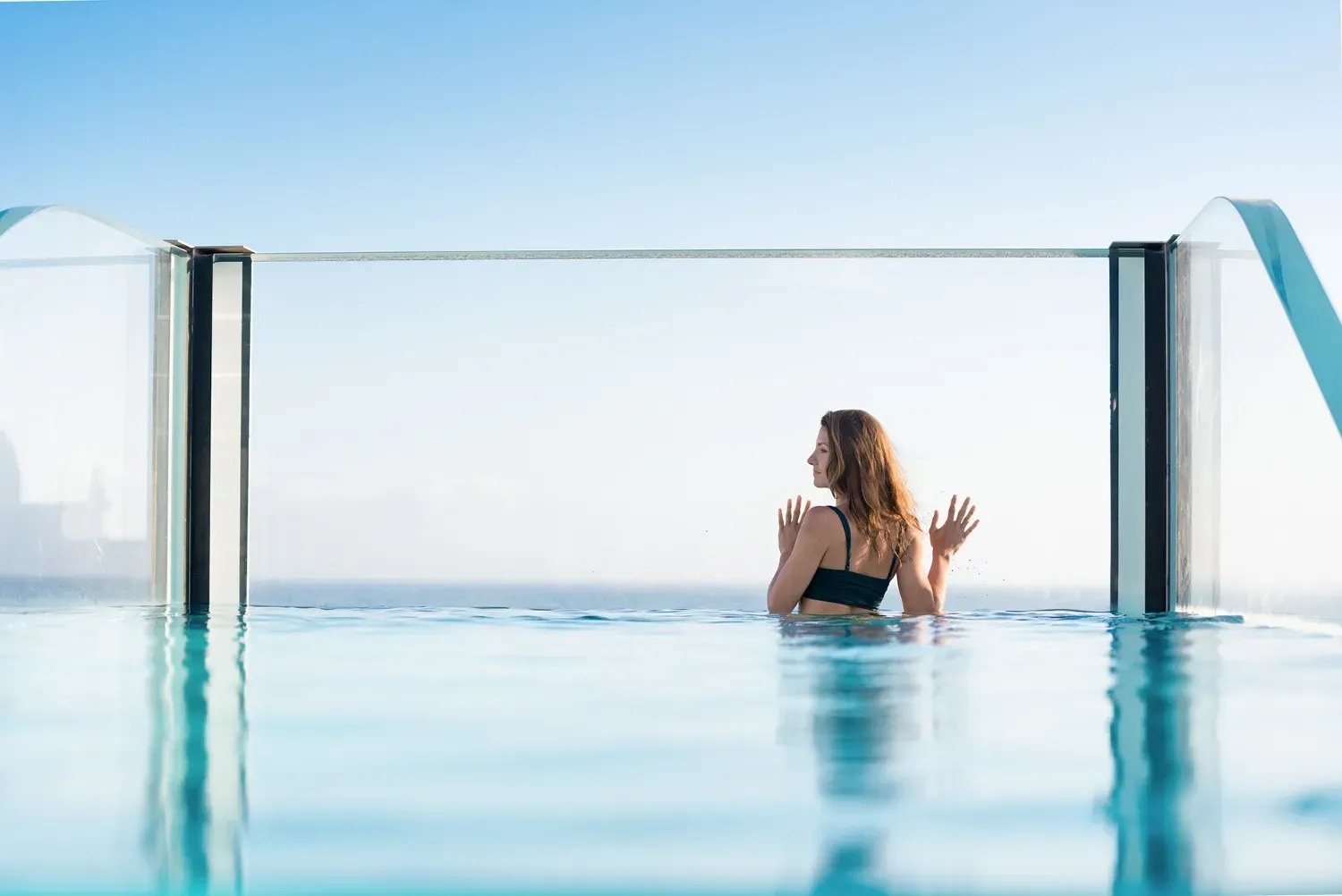 a woman in a black bikini is swimming in an infinity pool