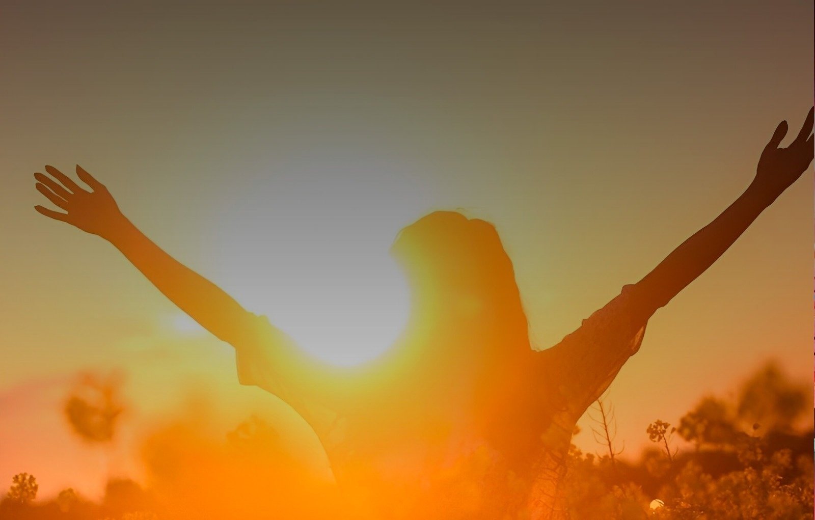 una mujer con los brazos extendidos en un campo al atardecer