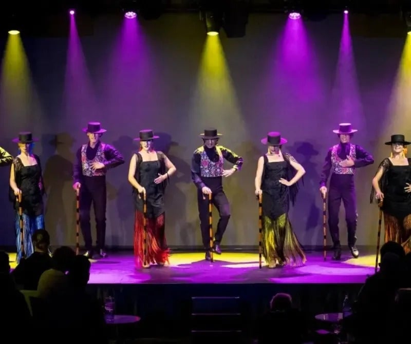 a group of people dancing on a stage with purple lights