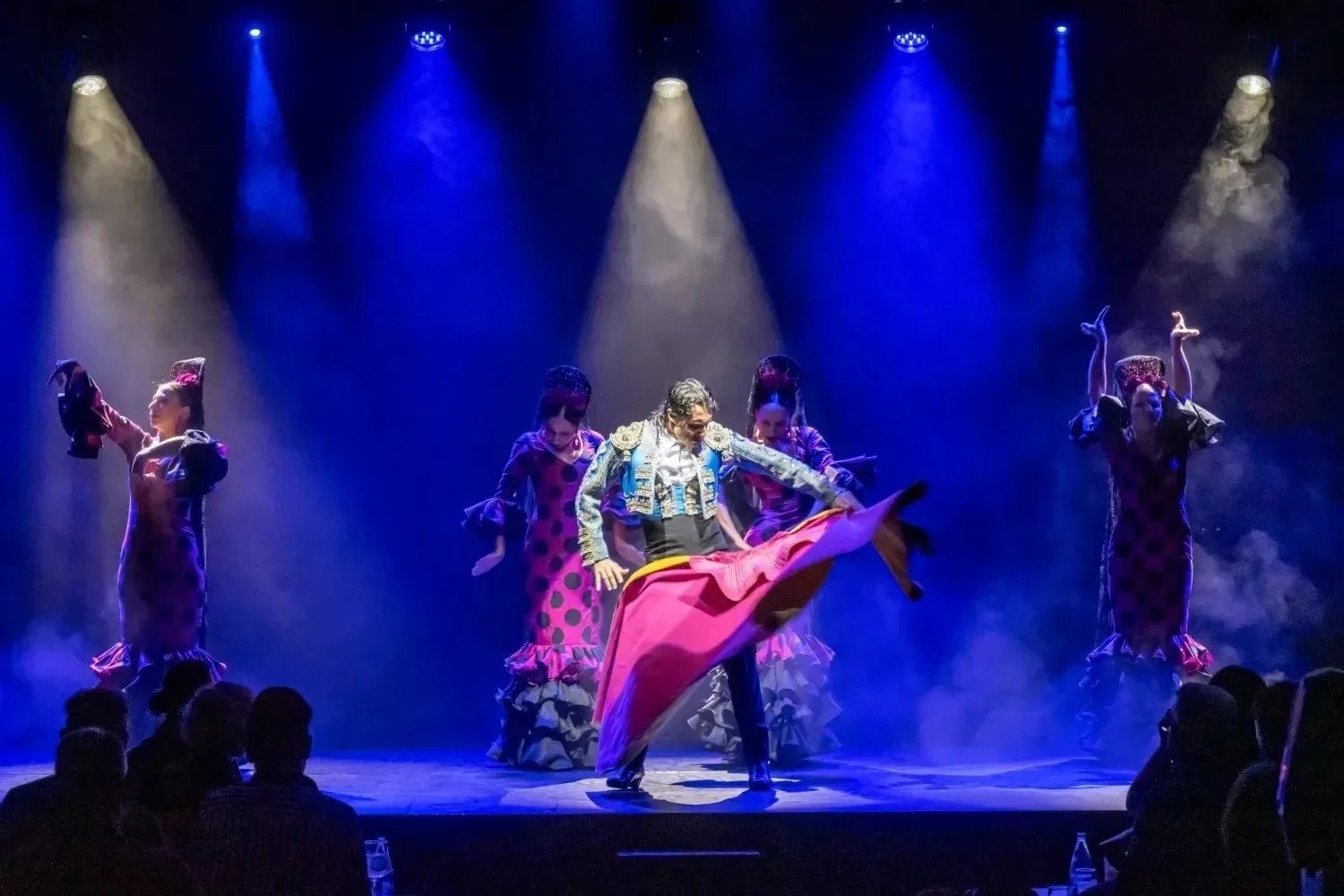 un grupo de hombres y mujeres en vestidos blancos con lunares rojos están actuando en un escenario