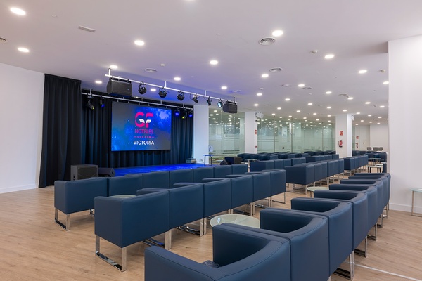 Sala de conferencias en GF: Victoria con mesas azules y sillas, vista al exterior.