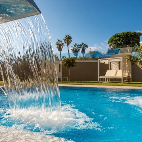 una cascada cae sobre una piscina con palmeras en el fondo