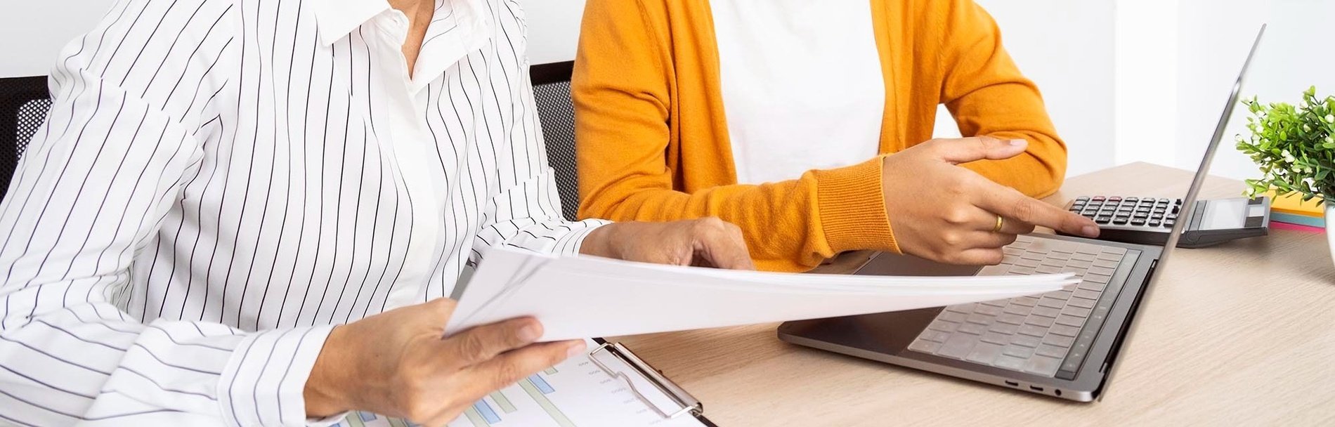 dos personas están sentadas en una mesa con una computadora portátil y un portapapeles