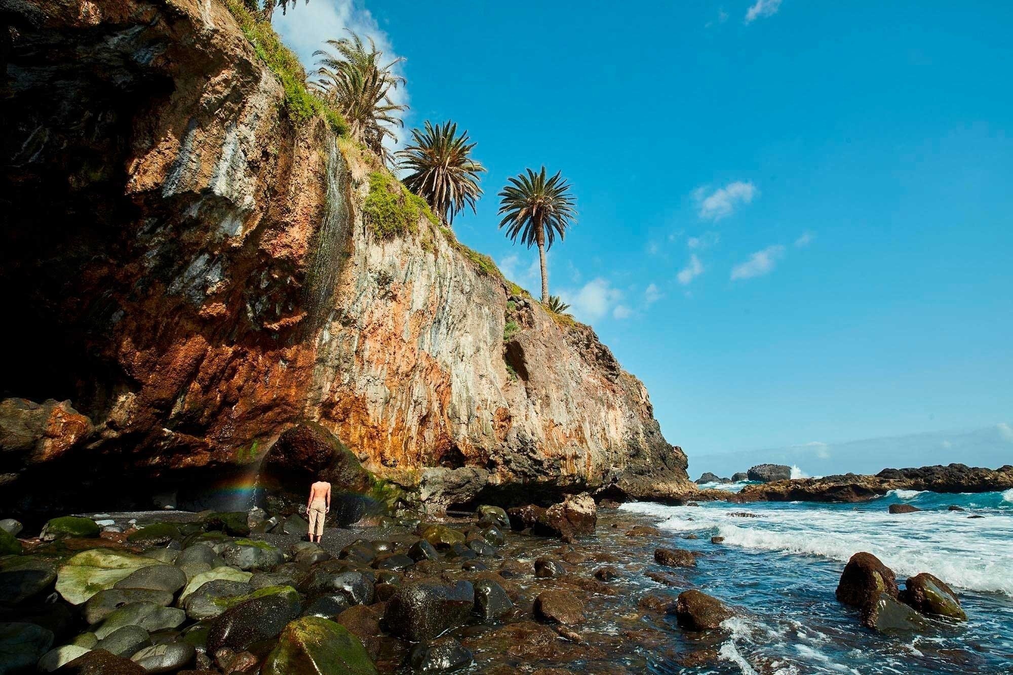 un hombre sin camisa está parado en una cueva junto al océano