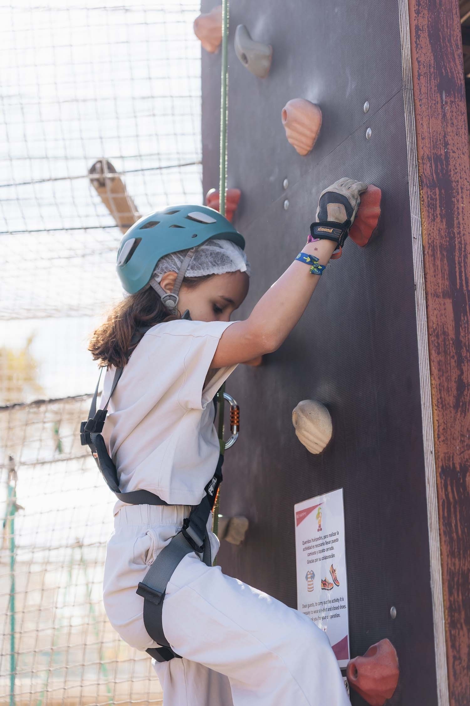 a little girl wearing a blue helmet is climbing a wall