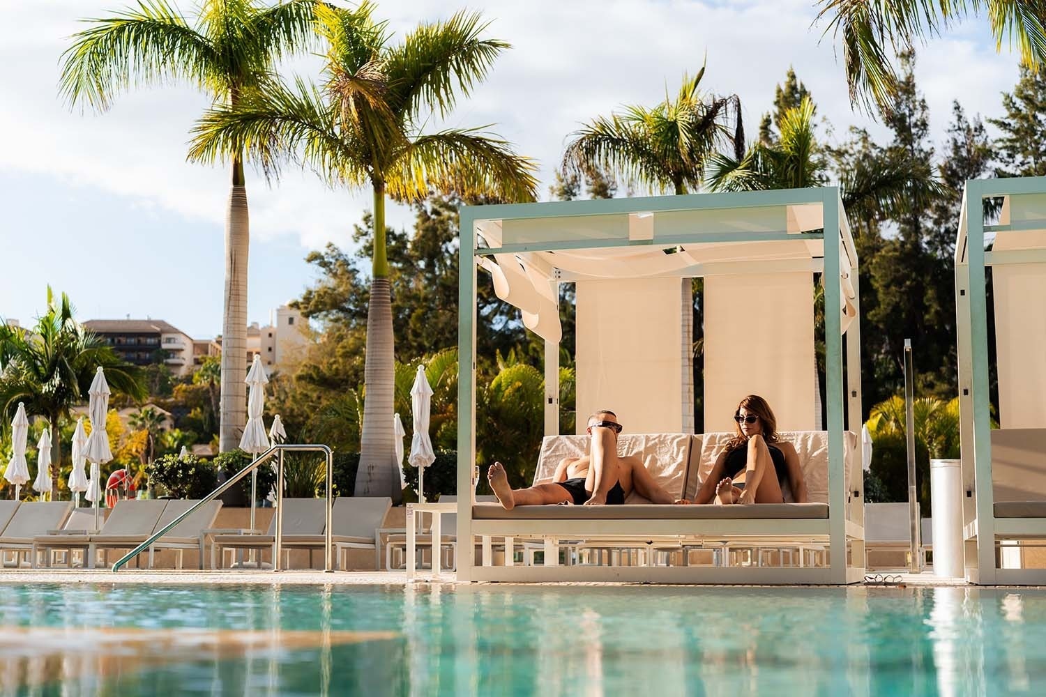 a man and a woman are laying under a canopy next to a swimming pool