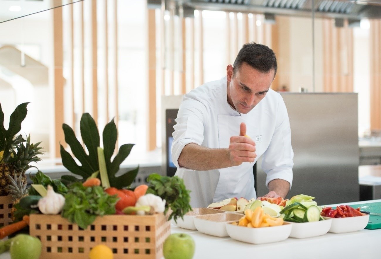 un chef da un pulgar hacia arriba mientras prepara un plato de frutas y verduras