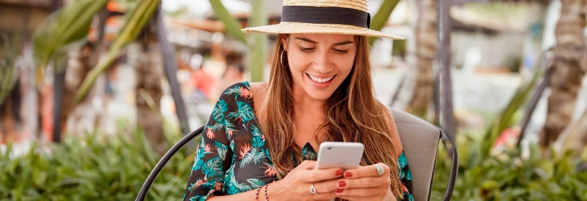 a woman wearing a straw hat is smiling while looking at her phone