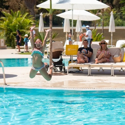 una niña salta en la piscina mientras un hombre y una mujer miran