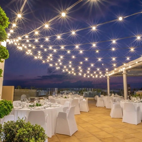 una terraza con mesas y sillas cubiertas con cubiertas blancas y guirnaldas de luces